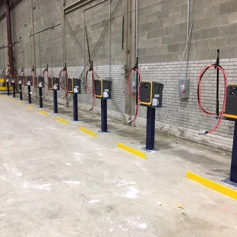 Row of industrial battery chargers on stands in warehouse facility with protective barriers