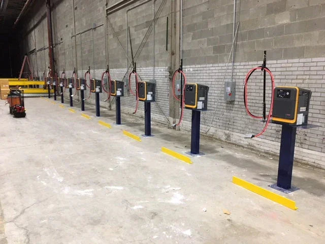 Row of industrial battery chargers on stands in warehouse facility with protective barriers