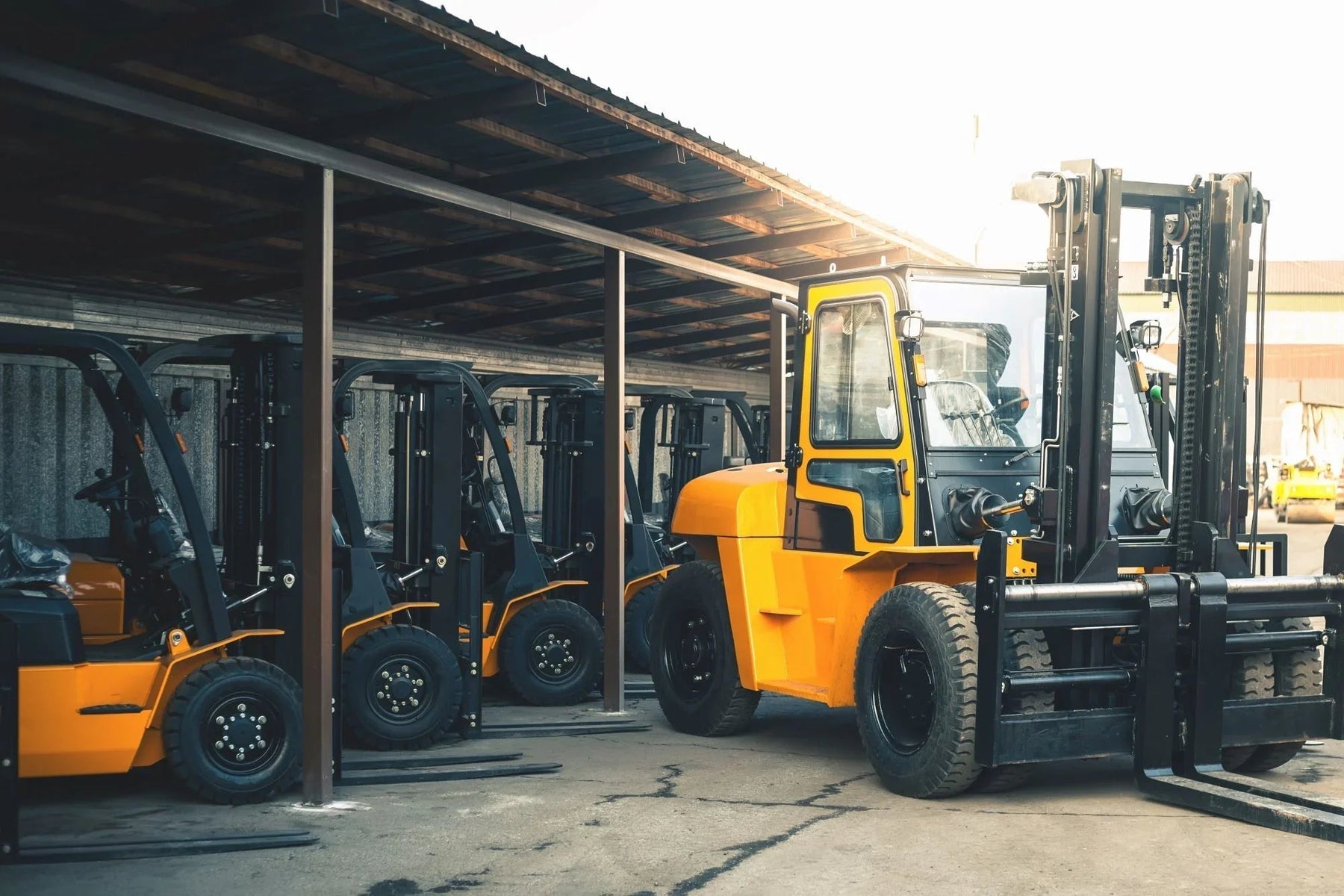 Multiple yellow forklifts parked under shelter in an industrial facility yard