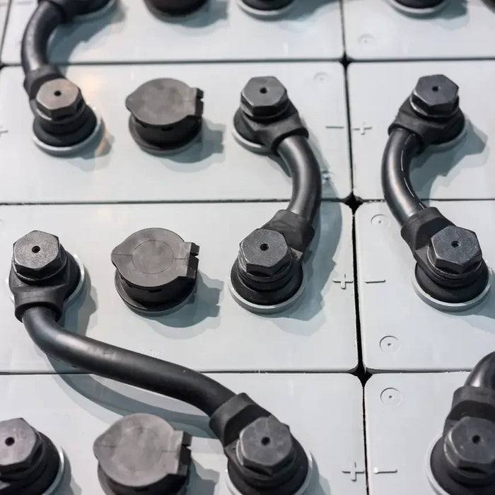 Close-up of industrial battery cells with black power cables connected.