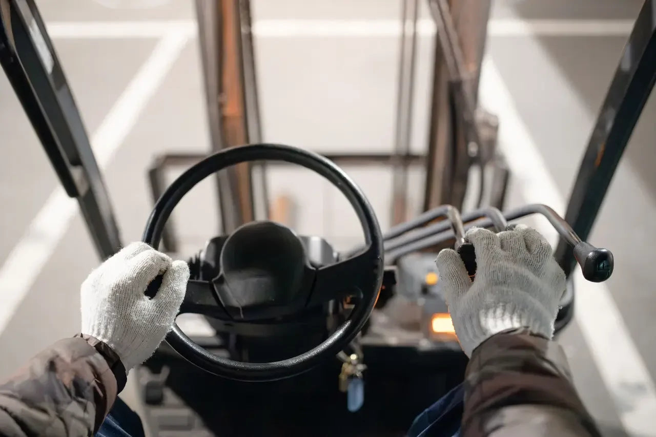 Operator hands on forklift steering wheel and controls, warehouse power equipment