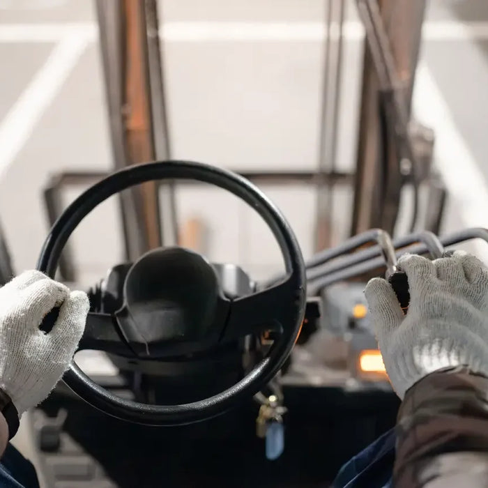Operator hands on forklift steering wheel and controls, warehouse power equipment