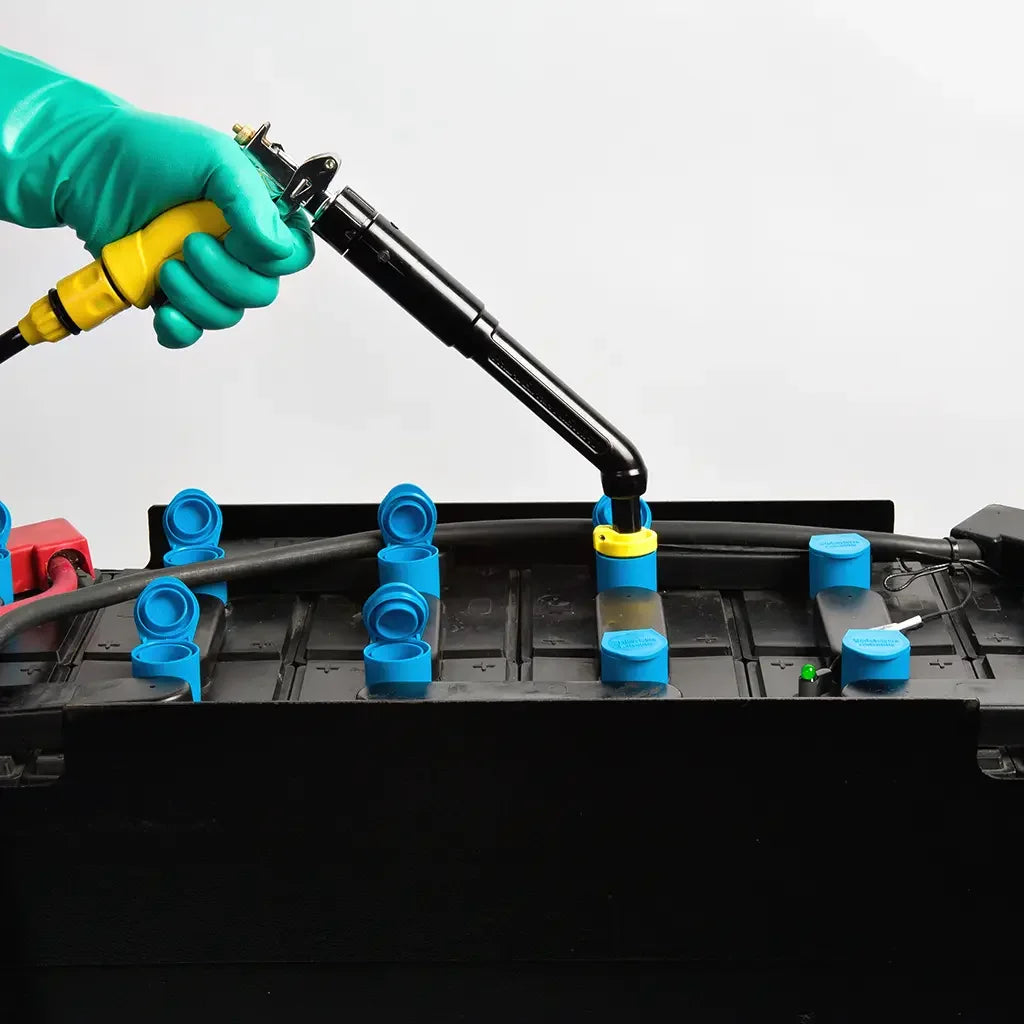 Hand with green glove using battery watering gun on industrial battery with blue caps